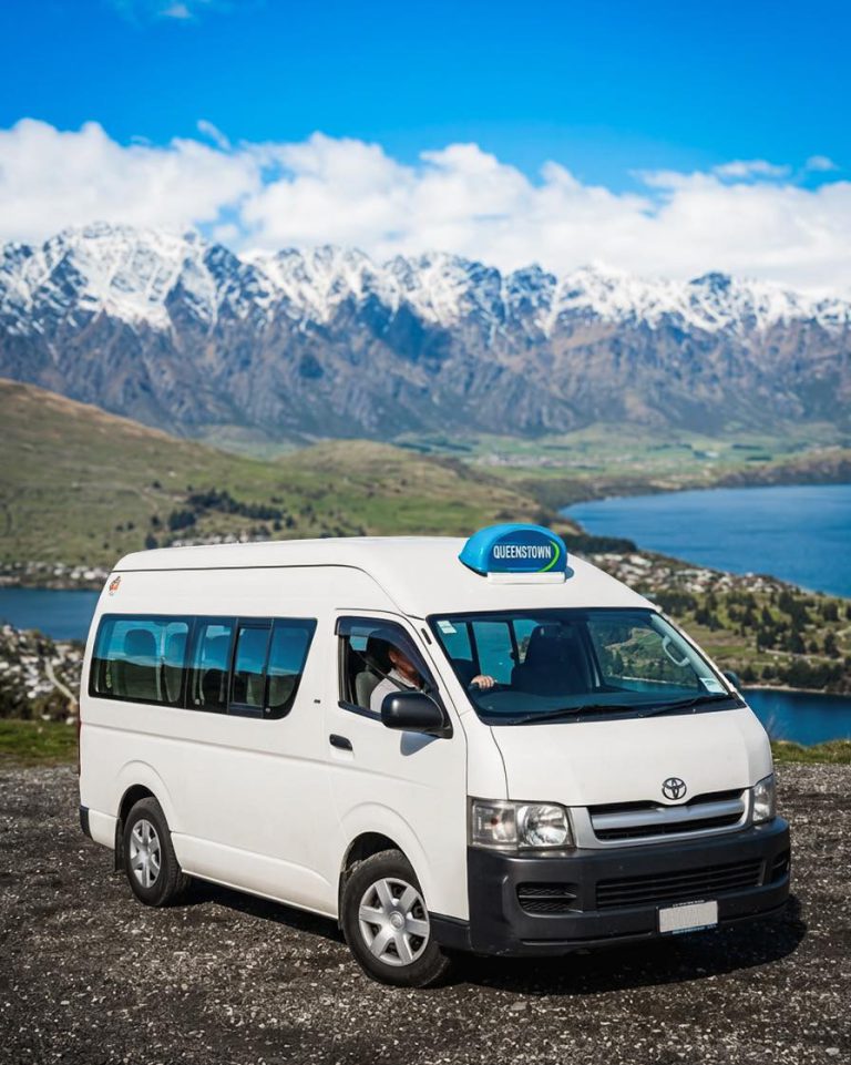 Queenstown Taxis van with its roof sign, in front of the snow-capped Remarkables